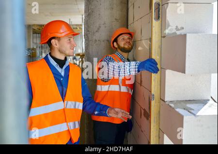 Costruttori di muratori che controllano il livello della parete con l'utensile Foto Stock