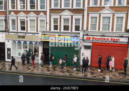 Londra, UK, 4 gennaio 2022: Sulla St John's Hill, vicino alla stazione di Clapham Junction, la gente si accaparrerà per le vaccinazioni in una clinica nonostante il clima freddo e piovoso. L'obiettivo del governo di dare a tutti gli adulti il loro colpo di richiamo prima della fine del 2021 non è stato raggiunto, ma farmacisti, GPS e centri specializzati di vaccinazione stanno ancora lavorando per vaccinare quante più persone possibile nella speranza di rallentare il tasso di infezioni omicron. Anna Watson/Alamy Live News Foto Stock