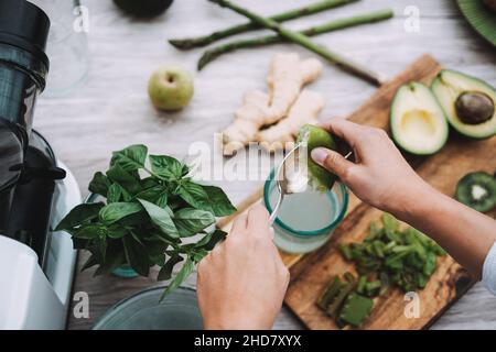 Giovane donna che prepara succo di disintossicazione con verdure e frutta verdi - Focus sulla mano sinistra Foto Stock