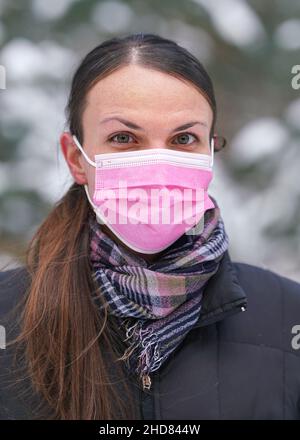 Giovane donna in giacca invernale con maschera monouso rosa virus del viso monouso Foto Stock