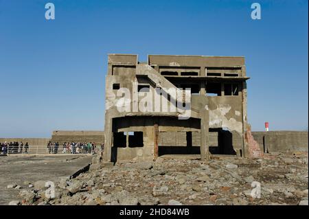 I turisti si trovano accanto a un edificio abbandonato sull'isola abbandonata di Hashima, conosciuta anche come Gunkanjima o isola della corazzata, vicino a Nagasaki, Giappone. Foto Stock
