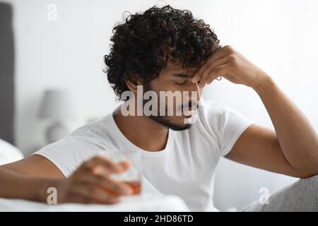 Uomo indiano depresso che beve alcool, interno della camera da letto, primo piano Foto Stock