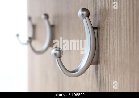 Tre appendiabiti di medie dimensioni color argento attaccati ad un asse di legno con focalizzazione sul primo. Attrezzatura per ingresso casa. Appendiabiti vicino Foto Stock