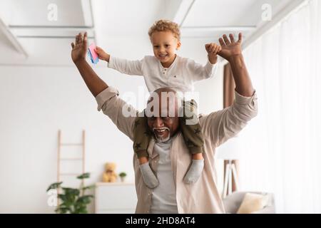 Grandpa allegra nera che trasporta il piccolo Grandson sulle spalle che giocano all'interno Foto Stock