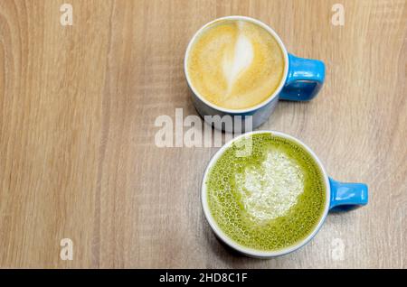 due tazze blu con cappuccino e tè matcha su un tavolo di legno Foto Stock
