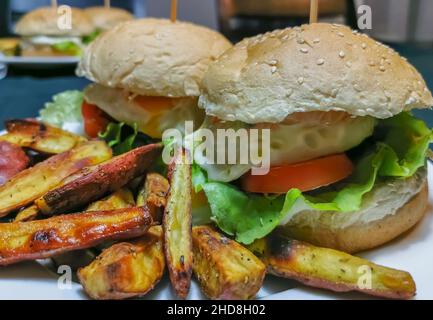 Vista di due hamburger vegetariani sul piatto, su un boccale con semi di sesamo, servito con tradizionale patata fritta dolce... Foto Stock