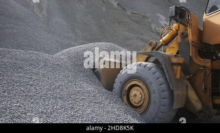 Il trattore raccoglie una paletta con ghiaia. Vista laterale di un escavatore che carica la benna con pietre o macerie schiacciate nel cantiere. Foto Stock