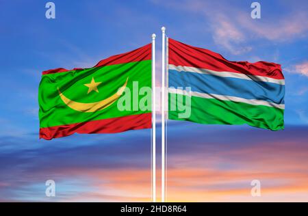 Mauritania e Gambia due bandiere su flagpoli e cielo nuvoloso blu Foto Stock