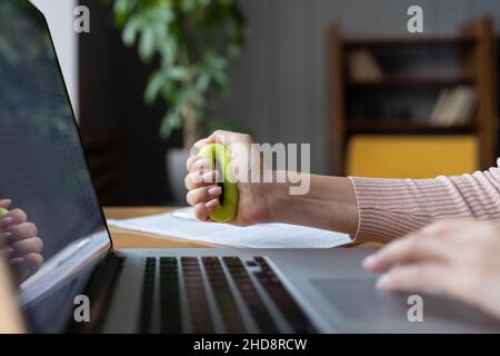Una donna d'affari o un lavoratore d'ufficio che afferra l'espansore in gomma mentre digita sul computer portatile Foto Stock