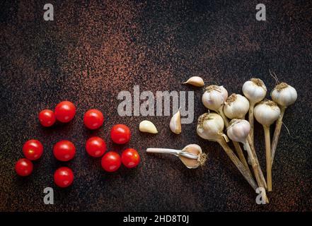 Piatto di pomodori ciliegini freschi con aglio su sfondo arrugginito scuro, vista dall'alto con spazio copia Foto Stock