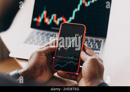 African man stock trader con smartphone con grafici finanziari e trading online dati di investimento Foto Stock