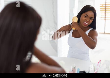 Donna Nera infelice Untagling i suoi capelli con Bamboo Brush in bagno Foto Stock