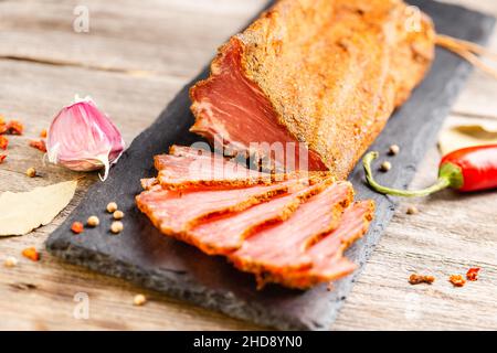 Tenderloin di maiale stagionato secco sul piano di servizio ardesia con aglio e peperoncino. Lonzino, antipasto con filetto a jerky su sfondo di legno. Foto Stock