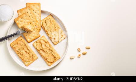 Burro di arachidi sparso su cracker di soda sul piatto visto dall'alto con coltello e sale. Vista dall'alto Foto Stock