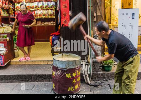 FENGHUANG, CINA - 13 AGOSTO 2018: Produttore di caramelle con mazzuolo in legno nella città vecchia di Fenghuang, provincia di Hunan, Cina Foto Stock