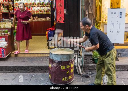 FENGHUANG, CINA - 13 AGOSTO 2018: Produttore di caramelle con mazzuolo in legno nella città vecchia di Fenghuang, provincia di Hunan, Cina Foto Stock