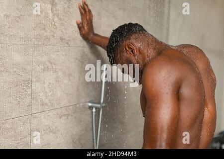 Black Man che prende la doccia in piedi sotto l'acqua rilassante in bagno Foto Stock