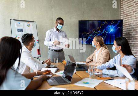 Covid Coworking. Uomo d'affari nero che indossa la maschera medica avere Ufficio riunione con i colleghi Foto Stock