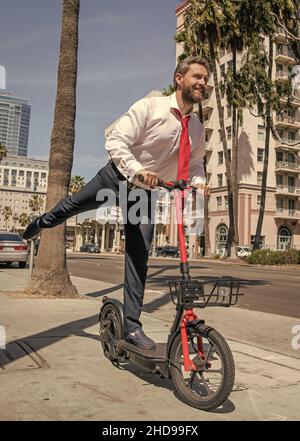 Ragazzo felice in formalwear ride stand-up e-scooter lungo il marciapiede, attivo Foto Stock