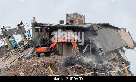 Attrezzatura pesante che è usata per strappare giù costruzione dell'edificio. Escavatore che lavora su un sito di demolizione Foto Stock