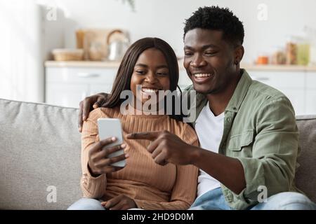 Felici gli amanti del nero che usano lo smartphone insieme, interni domestici Foto Stock
