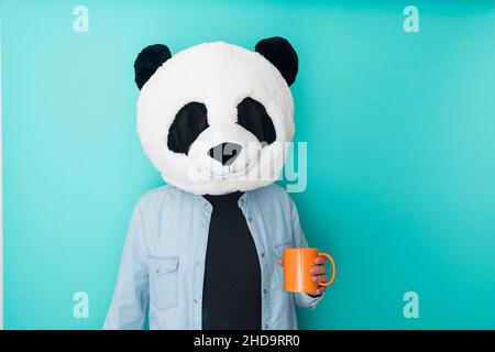 Persona in maschera panda che tiene una tazza di caffè su sfondo colorato Foto Stock