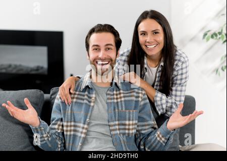 Ritratto di amorevole coppia caucasica, giovane uomo e donna, passare il tempo insieme, abbracciare a casa seduti sul divano in appartamenti moderni, guardando la macchina fotografica, sorridendo felicemente, armonico rapporto concetto Foto Stock