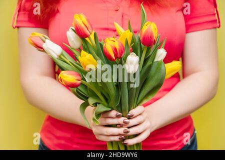 La giovane donna tiene nelle sue mani un grande bouquet di tulipani su sfondo giallo. Regalo per le vacanze primaverili. Foto Stock