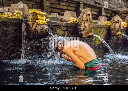 Uomo in primavera sacra acqua tempio di bali. Il tempio composto consiste di un petirtaan o struttura balneare, famoso per il suo santo acqua a molla Foto Stock