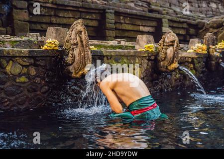 Uomo in primavera sacra acqua tempio di bali. Il tempio composto consiste di un petirtaan o struttura balneare, famoso per il suo santo acqua a molla Foto Stock