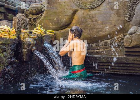 Uomo in primavera sacra acqua tempio di bali. Il tempio composto consiste di un petirtaan o struttura balneare, famoso per il suo santo acqua a molla Foto Stock