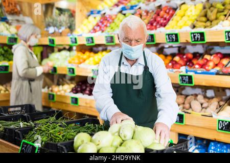 Il dipendente di un supermercato anziano che indossa una maschera protettiva lavora nell'area di vendita Foto Stock