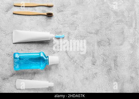 Tubi con pasta dentaria, spazzole e collutorio su sfondo grigio Foto Stock