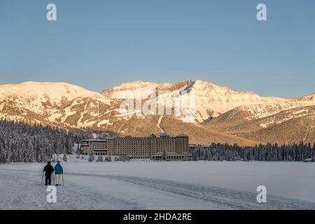 Lago Louise, AB, Canada-20 dicembre 2021: Coppia sci di fondo sul lago ghiacciato con Chateau Lago Louise e montagne innevate in backgroun Foto Stock