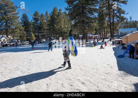Un uomo che cammina sulla neve con tubo di neve gonfiato verso la pendenza nel parco pubblico a Big Bear Lake, California, USA Foto Stock