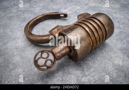 Lucchetto in ferro di tipo a vite di forma circolare vintage realizzato a mano con chiave su carta testurizzata Foto Stock