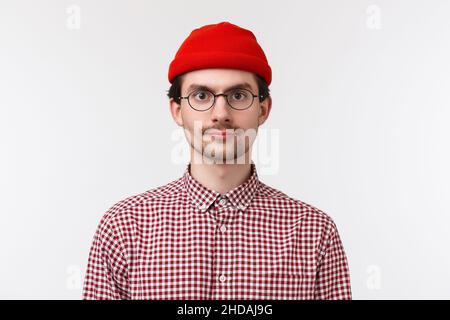 Primo piano ritratto di ragazzo hippster caucasico barbuto in occhiali e berretto rosso, camicia controllata, guardando macchina fotografica espressione casuale, concetto di persone Foto Stock
