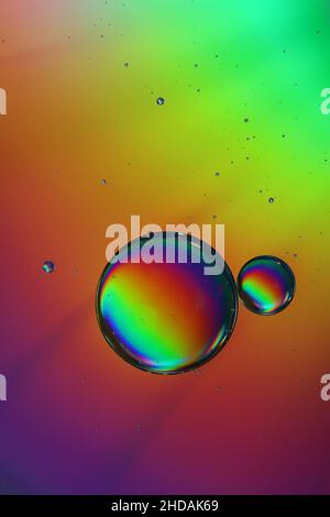 due goccioline d'olio si depositano su una superficie d'acqua e brillano nei bellissimi colori dell'arcobaleno Foto Stock
