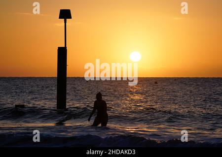 Un nuotatore esce dal mare mentre il sole sorge sulla spiaggia di Boscombe nel Dorset. Data foto: Mercoledì 5 gennaio 2022. Foto Stock