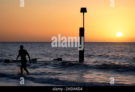 Un nuotatore esce dal mare mentre il sole sorge sulla spiaggia di Boscombe nel Dorset. Data foto: Mercoledì 5 gennaio 2022. Foto Stock