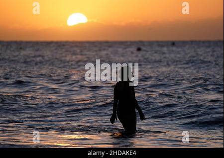 Un nuotatore si fa strada verso il mare mentre il sole sorge sulla spiaggia di Boscombe nel Dorset. Data foto: Mercoledì 5 gennaio 2022. Foto Stock