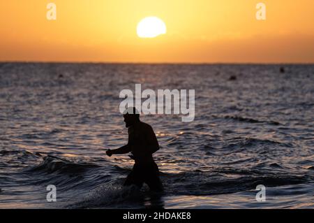 Un nuotatore esce dal mare mentre il sole sorge sulla spiaggia di Boscombe nel Dorset. Data foto: Mercoledì 5 gennaio 2022. Foto Stock