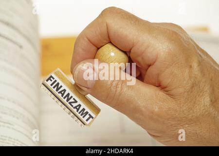 Eine Hand mit einem Stempel aus Holz, Aufschrift: Finanzamt, Steuererklärung, Lohnsteuer, Einkommenssteuer, Steuerprüfung, Foto Stock