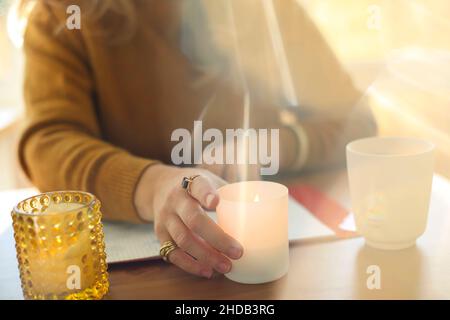 Immagine sfocata di donna seduta al tavolo che tiene bruciante candela profumata, femmina che crea l'atmosfera accogliente sul posto di lavoro. Pratica meditatio di consapevolezza Foto Stock