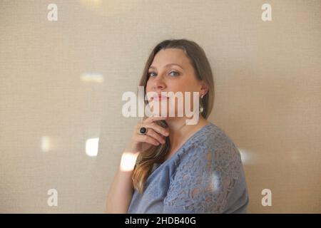 Amatevi ad ogni età. Donna di mezza età di 40s anni che tocca delicatamente il mento con la mano e guarda la macchina fotografica mentre si posa isolato su sfondo beige chiaro Foto Stock