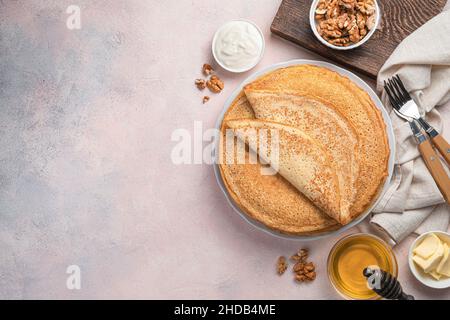 Pancake tradizionali con miele, panna acida e noci su sfondo rosa chiaro. Blini russi. Il concetto di Maslenitsa. Vista dall'alto, spazio di copia. Foto Stock