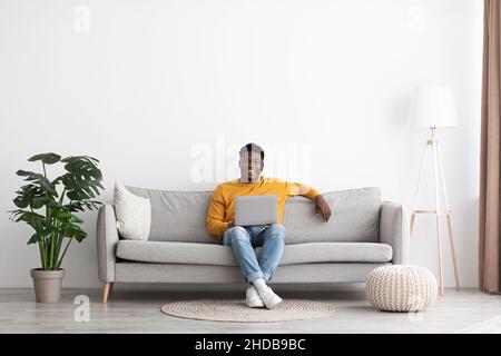 Ragazzo nero sorridente che si agghiacciava con il portatile a casa Foto Stock