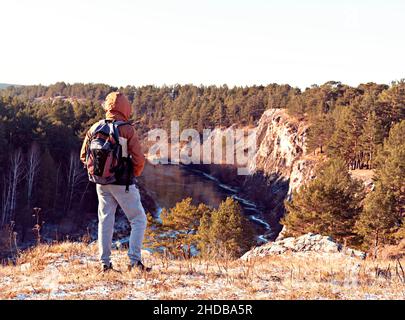 Vista posteriore del giovane uomo con zaino in piedi sulla montagna e guardando la vista del fiume in autunno o inverno escursioni bellezza in natura, stile di vita attivo Foto Stock