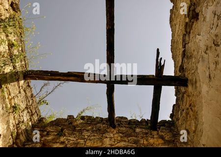 Antica struttura in pietra con resti di travi in legno. L'erba cresce sulle pareti. Vista dal basso, contro il cielo blu. Spazio di copia. Messa a fuoco selettiva. Foto Stock