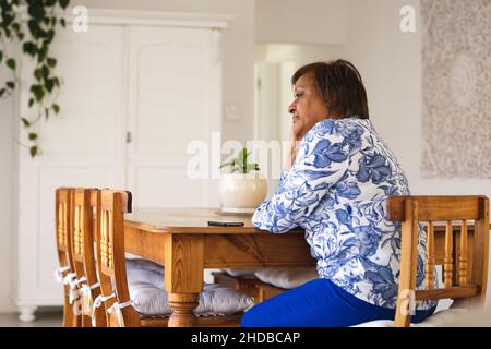 Triste afroamericana anziana guardare via mentre si siede al tavolo da pranzo Foto Stock
